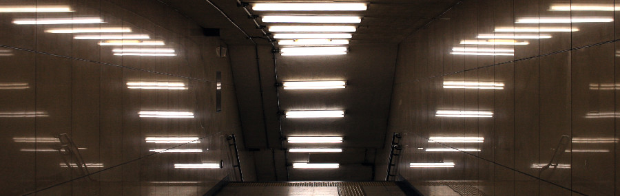 Bild eines Treppenabgangs mit Leuchtstoffröhren mit wenigen Farben, das eine trostlose Atmospähre ausstrahlt.